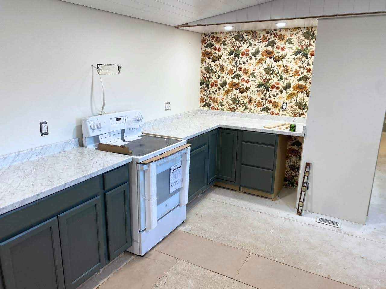 unfinished kitchen in a cottage with cabinets, countertops, wallpaper, and an oven