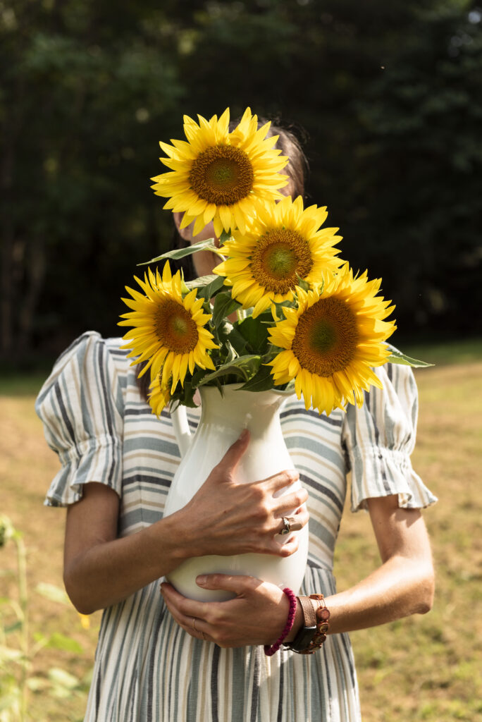 girl holding a vase and standing with sunflowers in front of her face